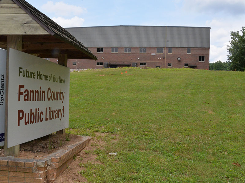 The new Fannin County Public Library will be located between this sign off Old Highway 76 and the Fannin County High School gym in the background.